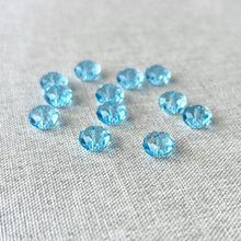 Load image into Gallery viewer, Close-up of multiple 8mm Aquamarine Austrian Rondelle Crystals - Aquamarine Blue scattered on a light textured fabric surface, showcasing their faceted sparkle and bright blue color.
