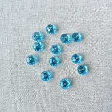 Load image into Gallery viewer, Scattered 8mm Aquamarine Austrian Rondelle Crystals - Aquamarine Blue with faceted surfaces on a neutral fabric background, displaying their bright blue color and sparkle.