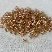 Load image into Gallery viewer, 6mm Light Colorado Topaz Austrian Bicone Crystals - Light Colorado Topaz Brown faceted beads scattered on a textured fabric surface for jewelry making projects.