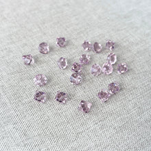 Load image into Gallery viewer, Scattered 6mm Light Amethyst Austrian Bicone Drop Crystals - Light Amethyst - Top Drilled - Package of 20 on a textured gray fabric background.