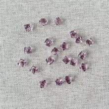 Load image into Gallery viewer, 6mm Light Amethyst Austrian Bicone Drop Crystals - Light Amethyst - Top Drilled - Package of 20 scattered on a light fabric background, showing their faceted surfaces and soft purple color.