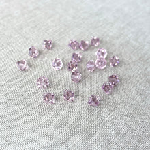 Load image into Gallery viewer, 6mm Light Amethyst Austrian Bicone Drop Crystals - Light Amethyst - Top Drilled - Package of 20 scattered on a neutral fabric surface, showing their faceted sparkle and soft purple color.