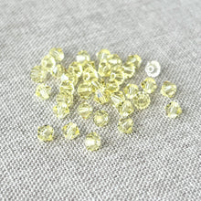 Load image into Gallery viewer, 4mm Jonquil CRYSTALLIZED™ Bicone Crystals - Jonquil Yellow - Pack of 37 scattered on a textured gray fabric background, showing their faceted, translucent yellow design.