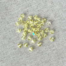 Load image into Gallery viewer, 4mm Jonquil CRYSTALLIZED™ Bicone Crystals in Jonquil Yellow, a pack of 37 faceted glass beads arranged on a textured neutral fabric background for jewelry making.