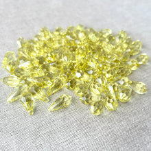 Load image into Gallery viewer, A pile of shiny yellow teardrop crystals scattered on a light fabric surface, showcasing the 15mm Jonquil CRYSTALLIZED™ Teardrop Drop Crystals - Jonquil Yellow - Top Drilled - Package of 97.