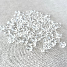 Load image into Gallery viewer, A close-up view of multiple 8mm Crystal Clear Austrian Round Crystals - Crystal Clear scattered on a light fabric background, showcasing their sparkling clarity and faceted design.