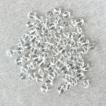 Load image into Gallery viewer, A collection of 8mm Crystal Clear Austrian Round Crystals - Crystal Clear scattered on a light fabric background, showcasing their faceted, sparkling surfaces.