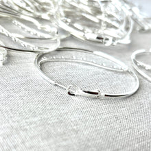 Load image into Gallery viewer, Close-up view of shiny silver hoop earrings with hinged closure resting on a light fabric surface, showcasing Silver Plated Steel 50mm Round Hoop Earrings - 9 Closed Loops - Hinged - 50 pairs.