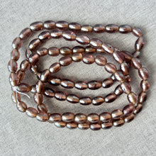 Load image into Gallery viewer, Rootbeer Glass Oval Beads - Pack of 2 - 16 inch strands - Translucent Glass in warm brown tones, arranged loosely on a neutral fabric background.