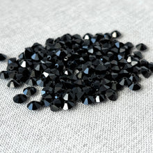 Load image into Gallery viewer, Close-up view of multiple Jet Black CRYSTALLIZED™ Austrian Faceted Rondelle Crystal - 6x4mm - Cut 5305 beads with deep black glossy facets on a textured light fabric background