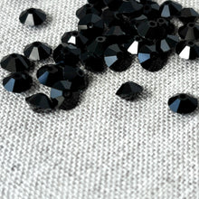 Load image into Gallery viewer, Jet Black CRYSTALLIZED™ Austrian Faceted Rondelle Crystal - 6x4mm - Cut 5305 scattered on a textured fabric surface, showcasing their deep black color and precision facets.