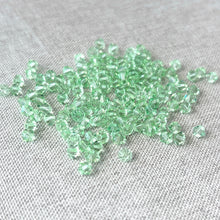 Load image into Gallery viewer, 4mm CRYSTALLIZED™ Austrian Bicone Crystals in Chrysolite Green, small faceted beads scattered on a light fabric surface, ideal for jewelry making and craft projects, Pkg of 136.