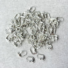 Load image into Gallery viewer, Pile of silver plated earwires with heart leverback clasps scattered on a light fabric surface, showing detailed craftsmanship of Heart Leverback Earwires - Silver Plated 18mm - Pack of 78 Earwires.