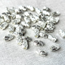 Load image into Gallery viewer, Swirl Diamond Cut Silver Plated Cylinder Beads Oval - Spacer Beads Metal Beads - Package of 48 scattered on a textured fabric background, showing reflective silver finish and detailed diamond cut swirl pattern.
