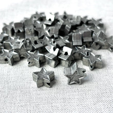 Load image into Gallery viewer, Close-up of multiple small silver star-shaped beads with holes, featuring Pewter Stars - 13mm Silver Pewter Stars Beads - Package of 40 beads arranged on a light fabric surface.