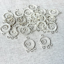 Load image into Gallery viewer, Small twisted silver spiral chandelier drops with three loops arranged on fabric, showcasing the Twisted Circle Spiral Chandelier Drop - 13mm Round 3 Loops - Sterling Silver - Package of 24.