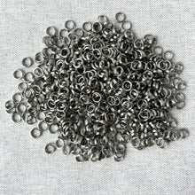 Load image into Gallery viewer, A close-up view of a large pile of shiny silver metal rings scattered on a textured surface, showcasing 5mm Rhodium Split Rings - Pack of 680 Splitrings used for jewelry making and crafts.