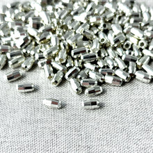 Load image into Gallery viewer, Silver Diamond Cut Oval Beads - 7mm x 4mm - Pkg of 240 - Spacer Beads Metal Beads scattered on textured fabric with shiny reflective surfaces.