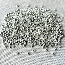 Load image into Gallery viewer, Round 3mm - Silver Plated - Spacer beads - Smooth Round - Ball Beads - Pack of 100 scattered on a textured fabric background with shiny silver finish.