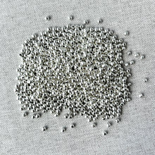 Load image into Gallery viewer, Round 3mm - Silver Plated - Spacer beads - Smooth Round - Ball Beads - Pack of 100 scattered on a light fabric surface, showing their shiny metallic finish ideal for jewelry making.