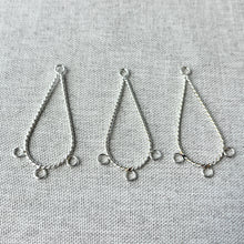 Load image into Gallery viewer, Three silver plated twisted teardrop-shaped chandelier drops each with three loops laid on a light fabric surface, Twisted Teardrop Chandelier Drop - 36mm Teardrop 3 Loops - Silver Plated - Package of 3.
