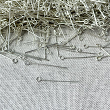 Load image into Gallery viewer, Pile of shiny silver plated eyepins with loops at one end scattered on textured fabric, displaying the Silver Plated 1" Eyepins - 24 Gauge - Pack of 3oz suitable for jewelry making and crafting.