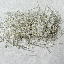 Load image into Gallery viewer, Close-up of numerous Silver Plated 1" Eyepins - 24 Gauge - Pack of 3oz scattered on a light fabric surface, used for jewelry making and crafting projects.