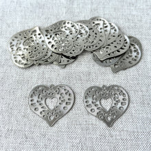 Load image into Gallery viewer, Drop, Lazer Lace™, silver-plated brass, 24x23mm fancy heart pieces with intricate cut-out design, displayed on a textured fabric background, sold per pkg of 20.