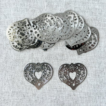 Load image into Gallery viewer, Drop, Lazer Lace™, silver-plated brass, 24x23mm fancy heart pieces featuring intricate cutout patterns, arranged on a light fabric background, sold per pkg of 20.