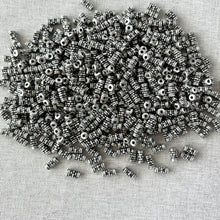 Load image into Gallery viewer, Antique Silver - 7mm x 3mm - Tube with Beaded Flower beads scattered on a textured fabric surface, showcasing detailed floral and beaded design perfect for jewelry making.